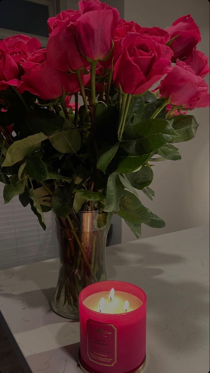 a vase filled with pink roses next to a lit candle