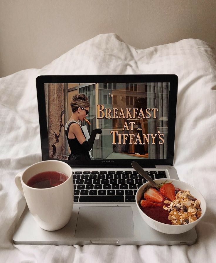 an open laptop computer sitting on top of a bed next to a bowl of cereal