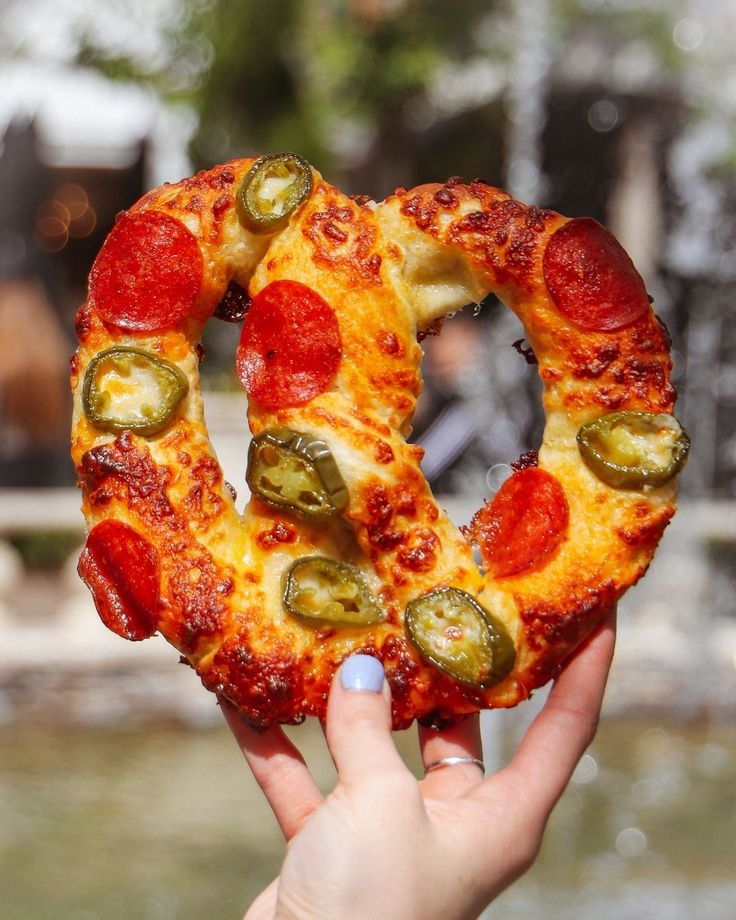 a person holding up a pizza ring with pepperoni and jalapenos on it