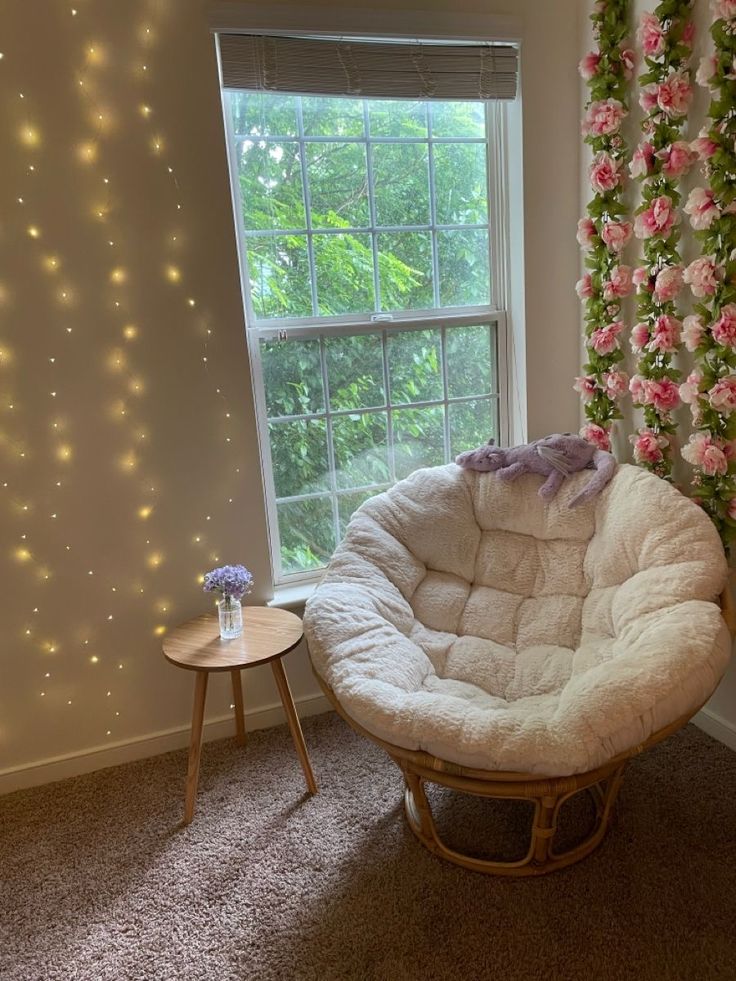 a white chair sitting in front of a window next to a table with flowers on it