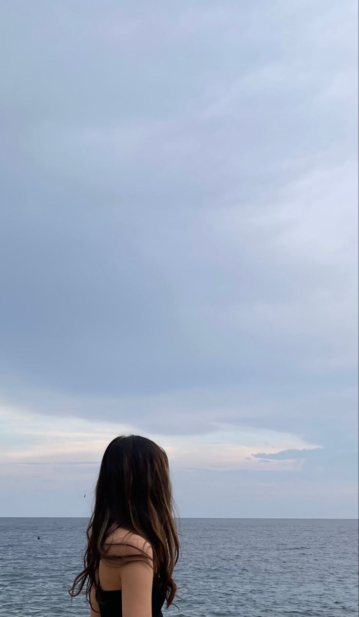 a woman standing on top of a beach next to the ocean under a cloudy sky