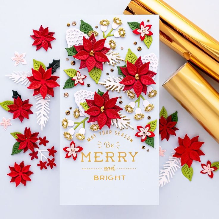 a christmas card with poinsettis and gold foil on the bottom, surrounded by other holiday decorations