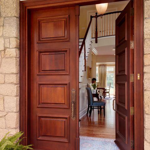 an open wooden door leading to a living room and dining area with stairs in the background