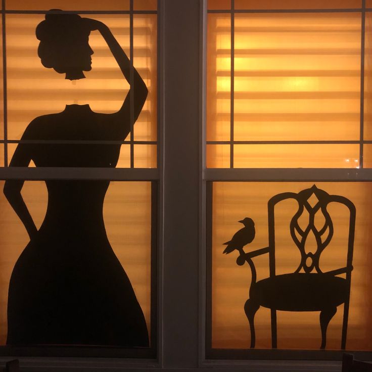 a silhouette of a woman standing in front of a window next to a chair with a bird on it