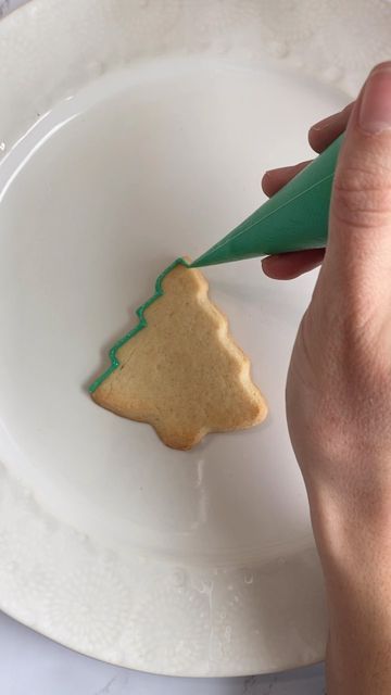 a person is decorating a small christmas tree cookie on a plate with a green marker