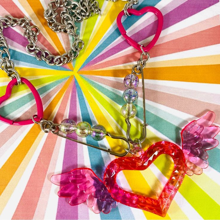 two heart shaped keychains with angel wings on a multi - colored striped background