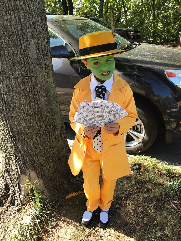 a child in a yellow suit and top hat holding money standing next to a tree