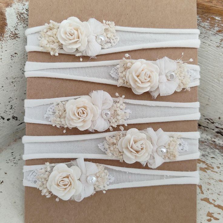 three wedding garters with white flowers and pearls on brown paper, sitting on a wooden surface