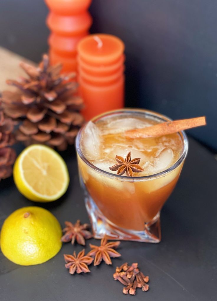 a drink with an orange and cinnamon garnish sits on a table next to pine cones