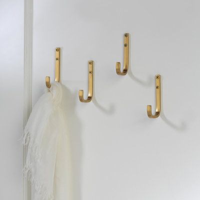 three gold hooks hang on a white wall next to a scarf and coat rack with two scarves