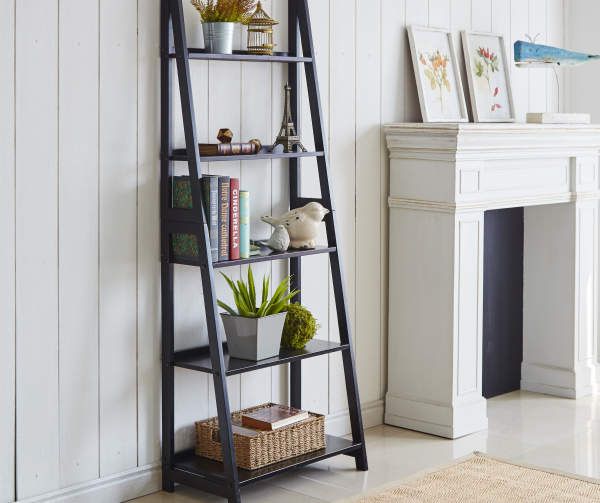 a black leaning shelf with books and plants on it in front of a white fireplace