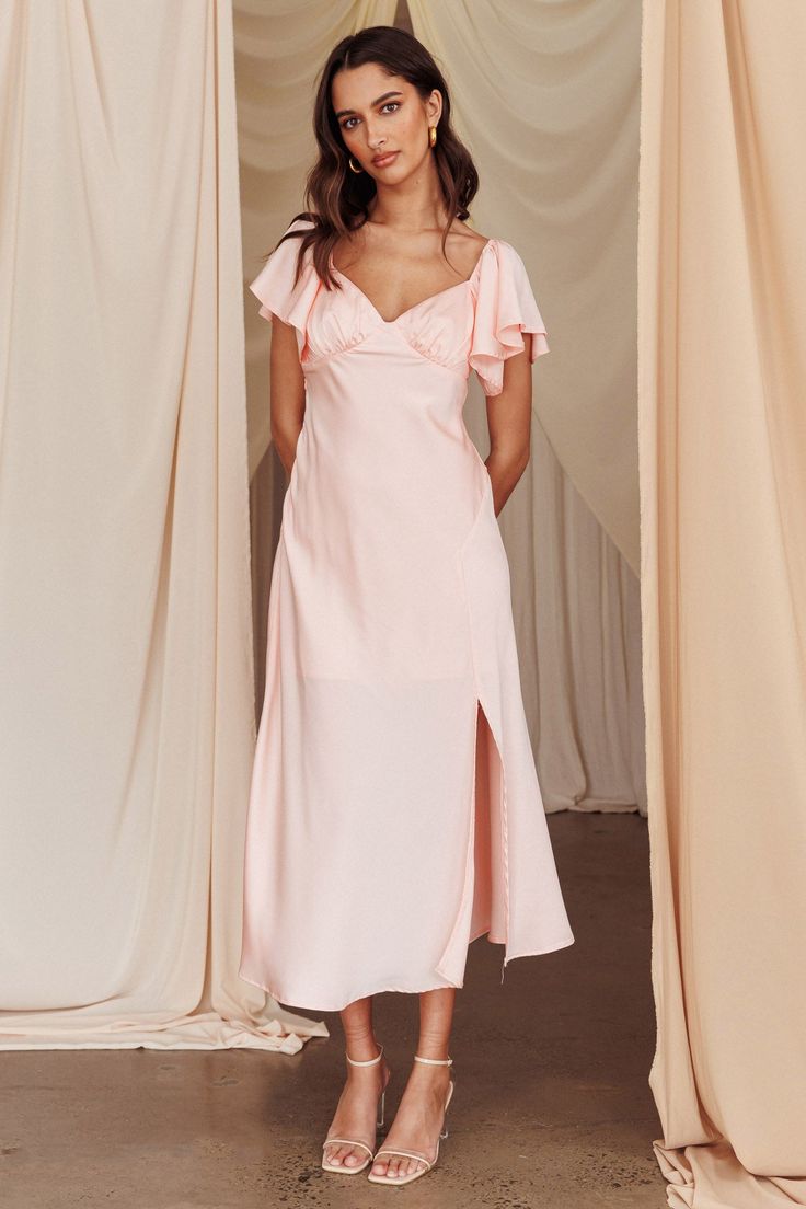 a woman standing in front of curtains wearing a pink dress with ruffles on the shoulders