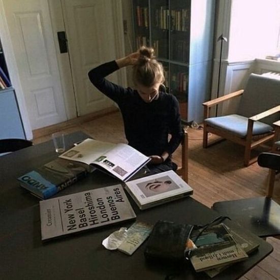 a woman sitting at a table with several books on top of it in front of a bookcase