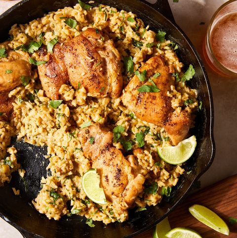 chicken and rice in a skillet with lime wedges next to glasses of beer