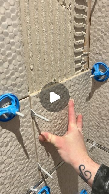 a person is holding scissors in front of a wall with holes cut into the tiles