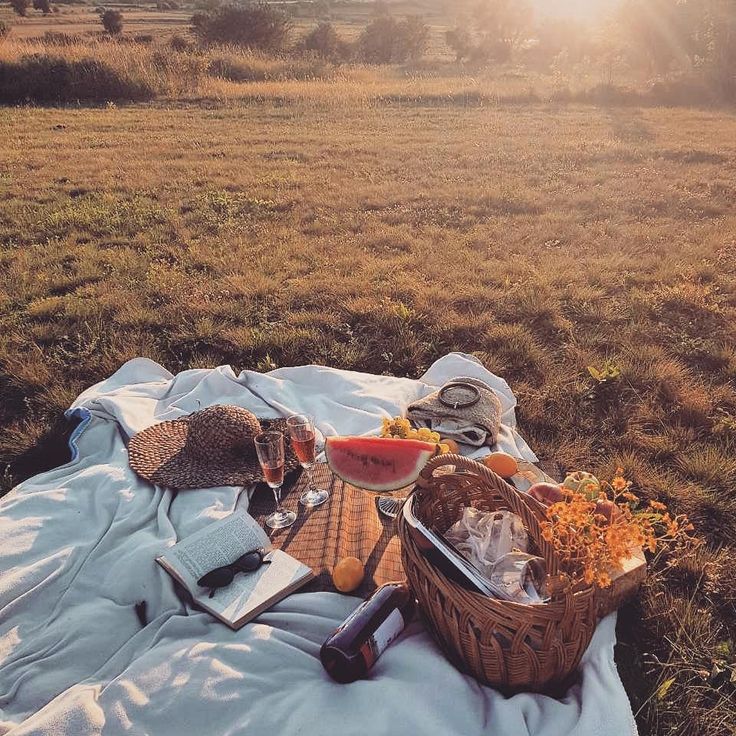 a picnic blanket with food on it in the middle of an open grassy field at sunset