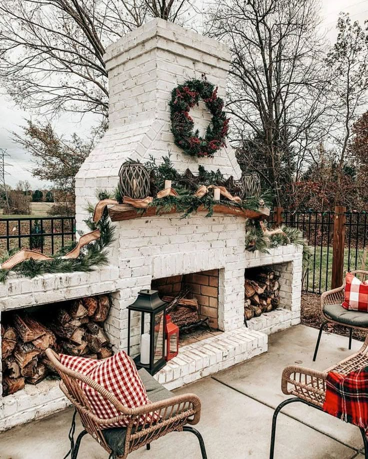 an outdoor fireplace decorated for christmas with wreaths on top and firewood in front