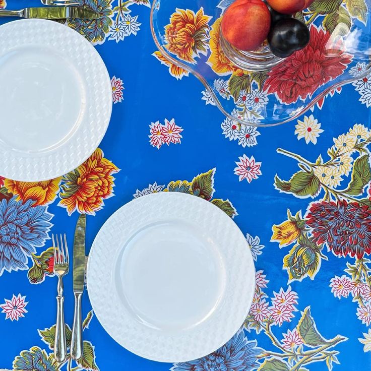 two white plates on a blue floral table cloth with fruit and silverware in the background