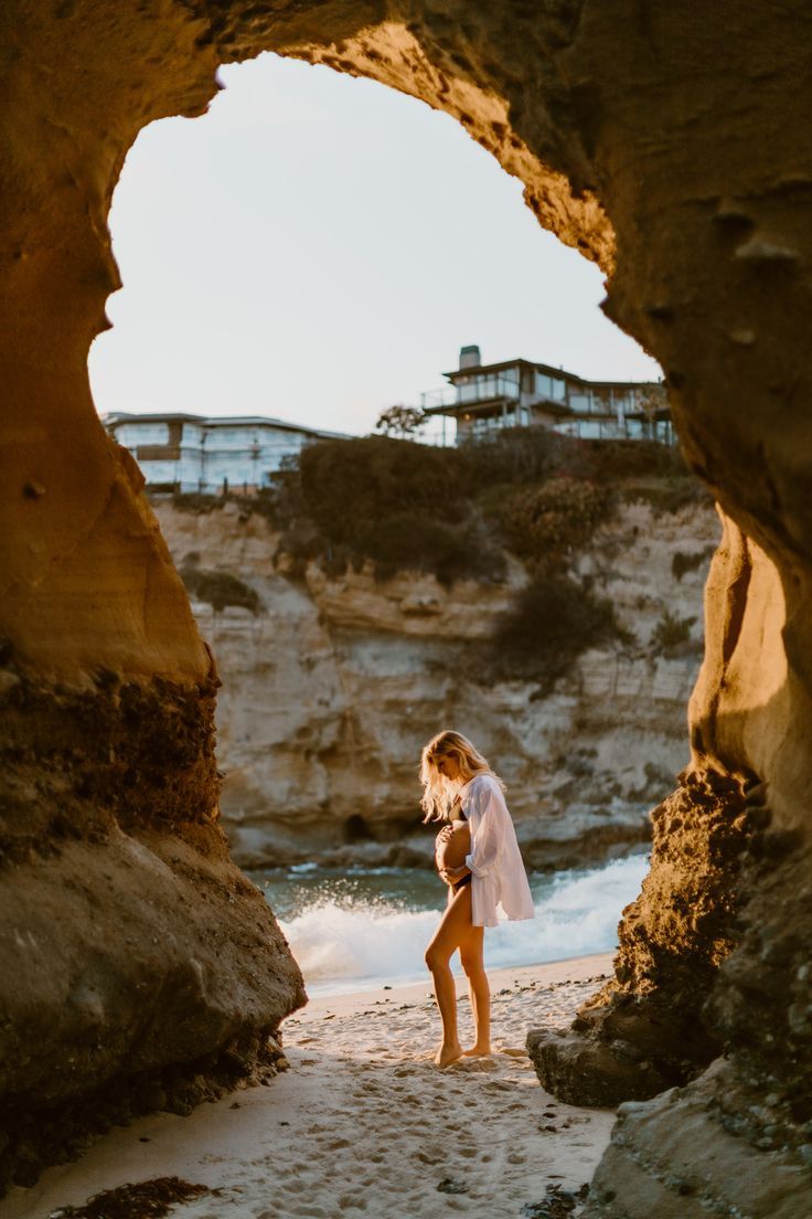 a woman standing on top of a sandy beach next to the ocean under an arch