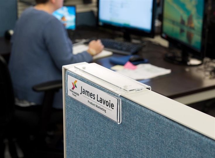 a person sitting at a desk in front of two computer monitors and a keyboard with the name james lavoie on it