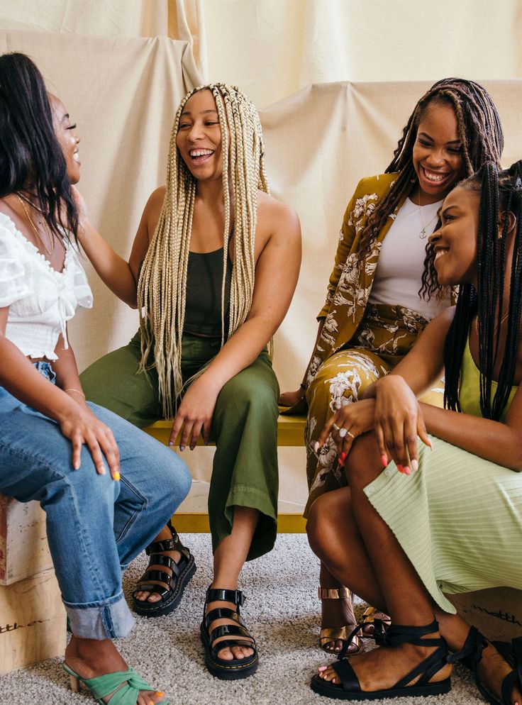 three women sitting on a couch laughing and having fun with their hair in braids