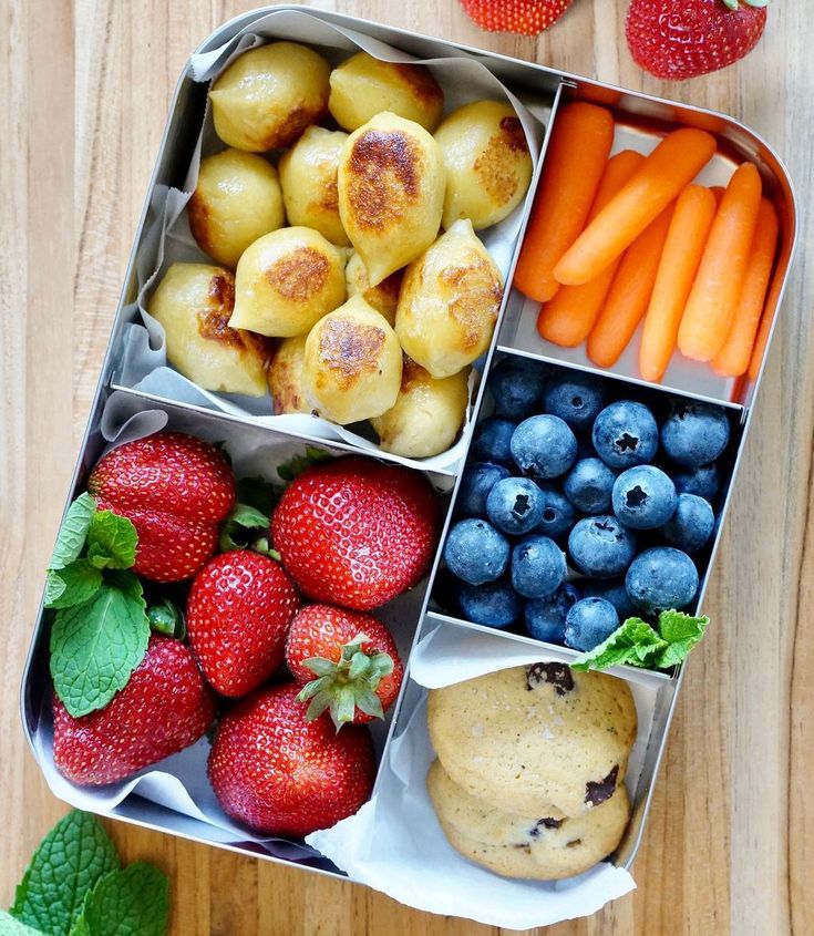 an open lunch box filled with fruit and veggies on top of a wooden table