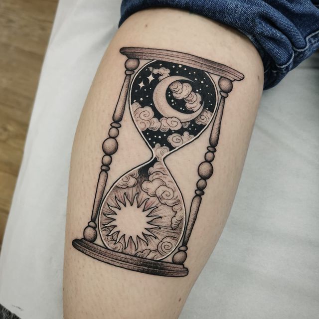 an hourglass tattoo on the leg with stars and moon in it, sitting on a person's arm