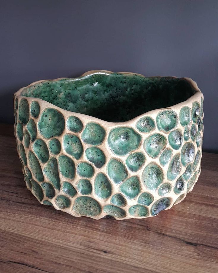 a green ceramic bowl sitting on top of a wooden table next to a gray wall