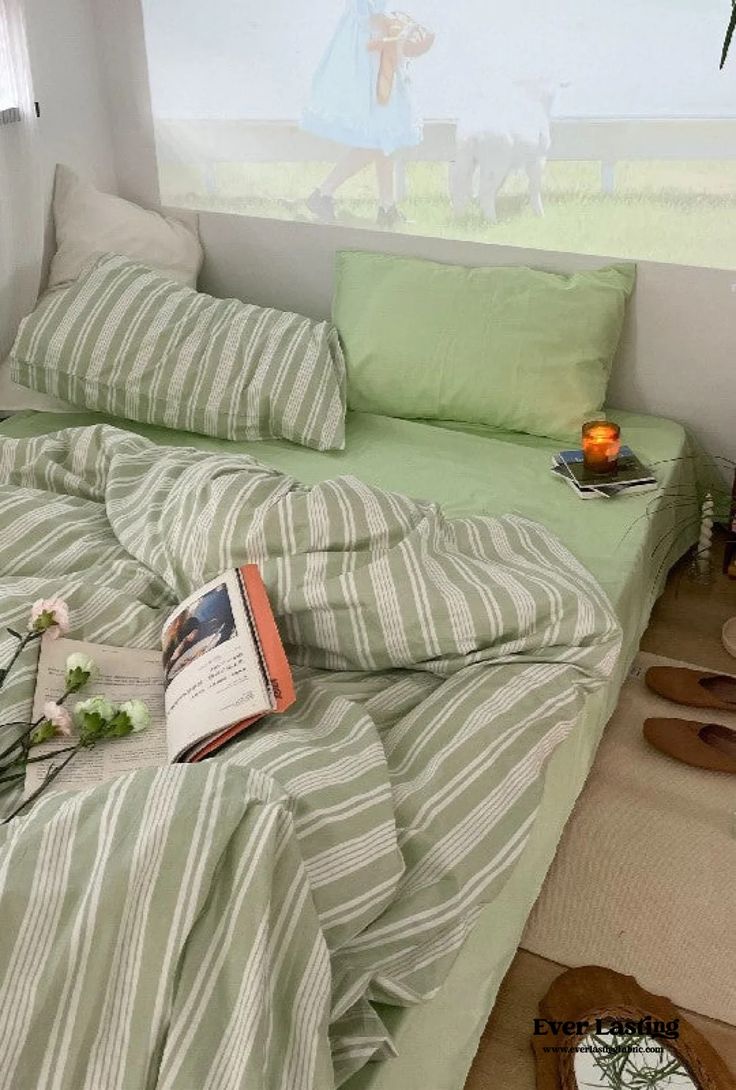 a bed with green and white striped sheets in a bedroom next to a painting on the wall