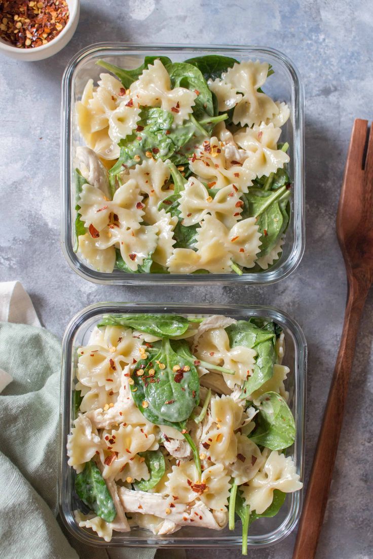 two plastic containers filled with pasta salad next to wooden utensils on a table