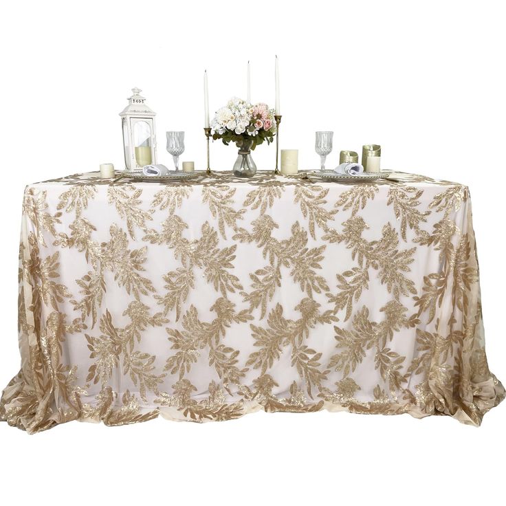 a table topped with candles and flowers on top of a white table cloth covered in gold leaves