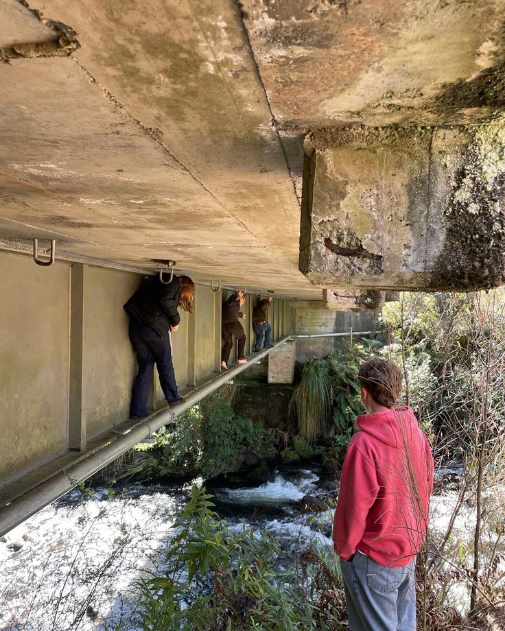 two men are standing on the side of a bridge and looking down at water below