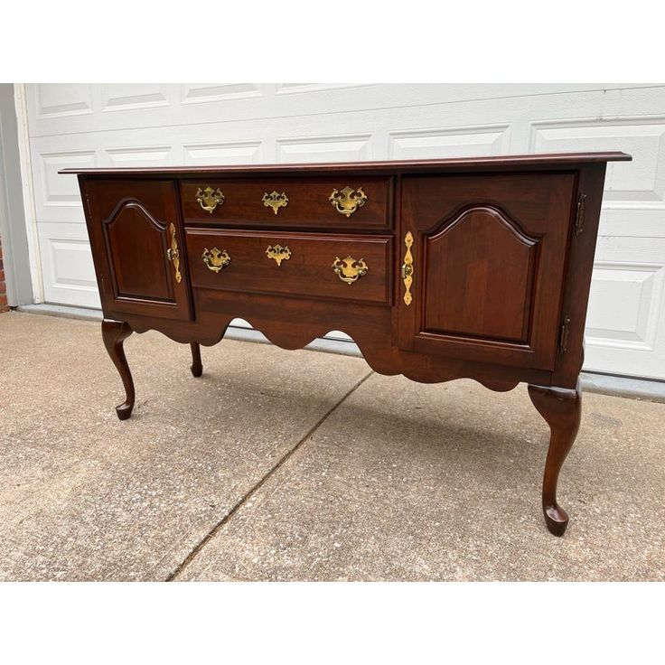 an old wooden sideboard with gold decorations on the top and bottom, sitting in front of a garage door