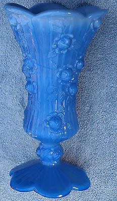 a blue glass vase sitting on top of a table next to a white wallpaper