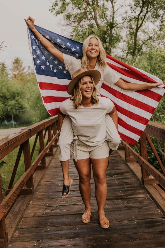 two women walking across a bridge with an american flag on their shoulders and one holding the other