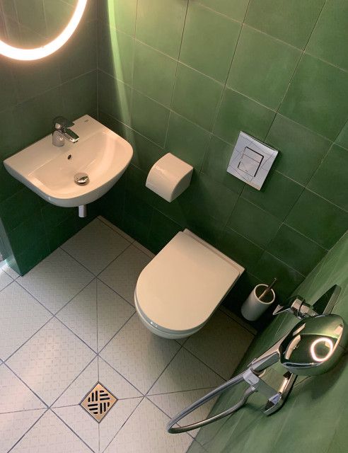 a bathroom with green tiles and a white toilet next to a sink under a mirror