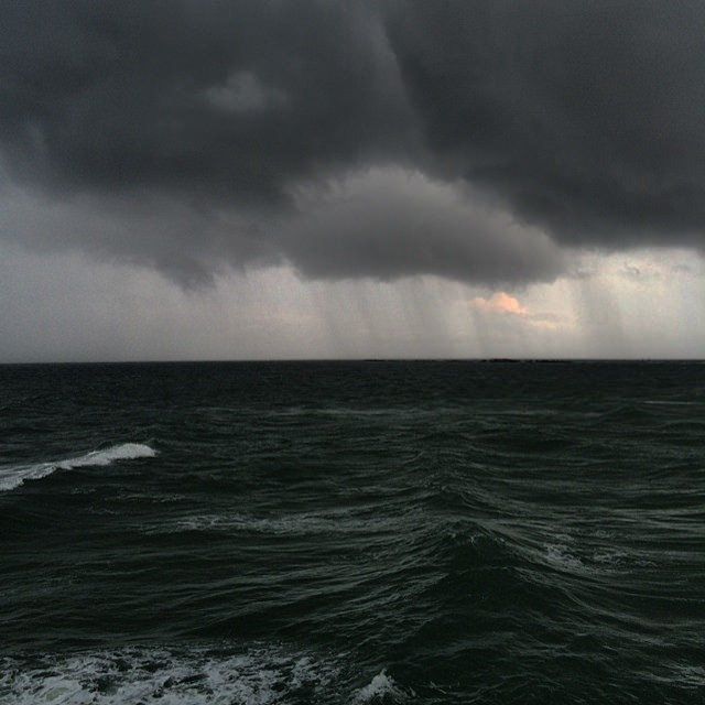 storm clouds over the ocean with a boat in the distance under dark gray skies and sunbeams