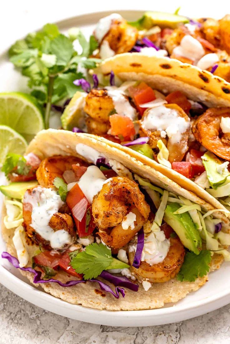 two shrimp tacos with lettuce, tomatoes and cilantro on a white plate