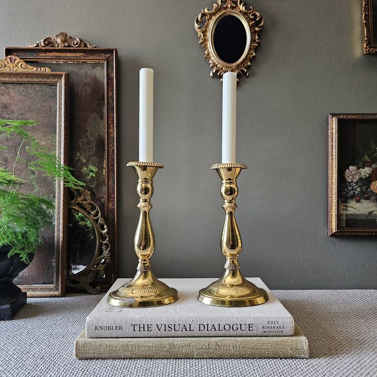 two gold candlesticks sitting on top of a book in front of a mirror