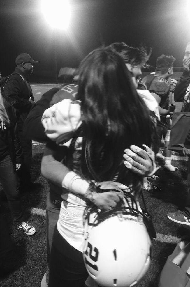 a football player is hugging his girlfriend on the sidelines at a game in black and white