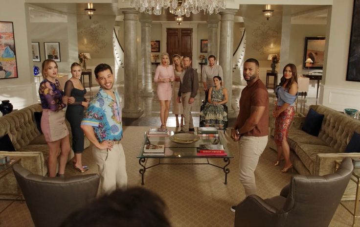 a group of people standing in a living room next to couches and coffee tables