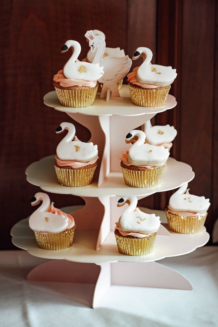 cupcakes with swans on them sitting on a three tiered cake stand