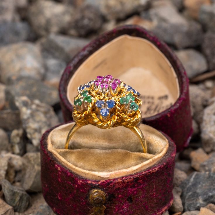 This vintage floral ring features clusters of emeralds, rubies, and sapphires that are accented with a gold rope motif. The ring is crafted in 18k yellow gold with a rich patina. It is currently a size 6.25. Several of the stone have a bit of light wear. Antique Multi-stone Yellow Gold Cluster Ring, Antique Multi-stone Cluster Ring In Yellow Gold, Antique Gold Cluster Ring With Multi-stone, Yellow Gold Multi-stone Cluster Sapphire Ring, Yellow Gold Cluster Multi-stone Sapphire Ring, Vintage Gold Multi-stone Cluster Ring, Cluster Emerald Ring In Yellow Gold With 17 Jewels, Heirloom Multi-stone Cluster Ring, Heirloom Yellow Gold Multi-stone Sapphire Ring