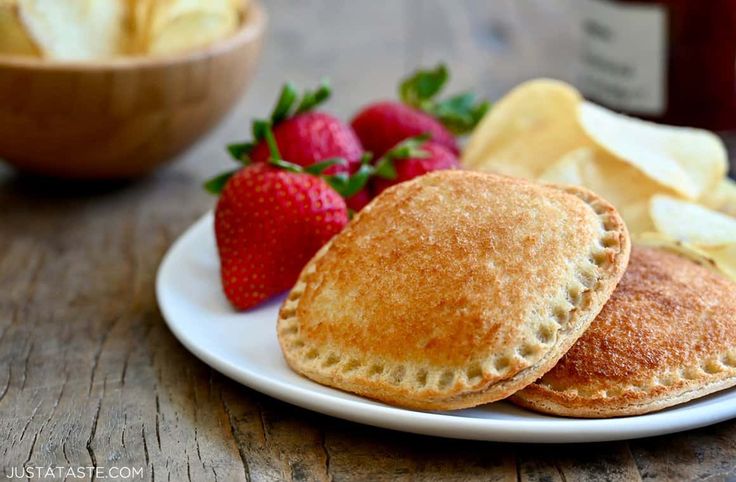 two pancakes on a plate with strawberries and apple slices next to the bowl of fruit