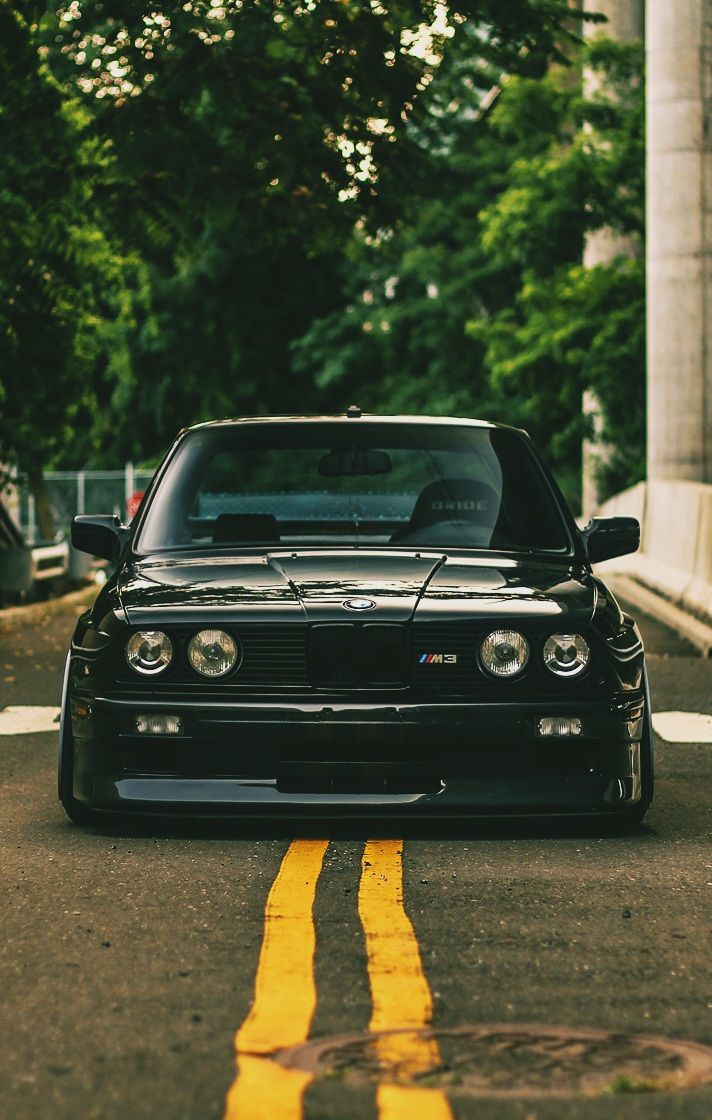 a black car parked on the side of a road next to a yellow line with trees in the background