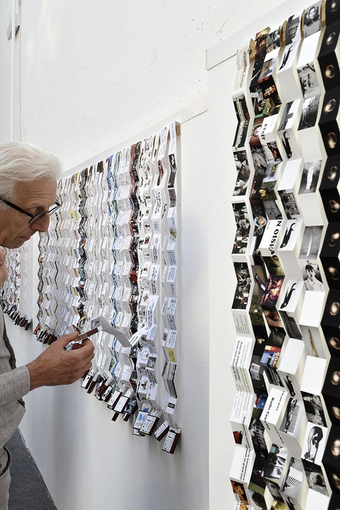 an older man is looking at photos on the wall with glasses hanging from it's sides