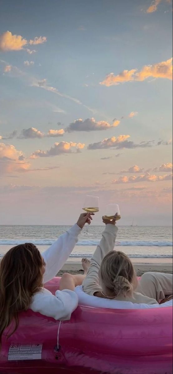 two women sitting on an inflatable boat at the beach, one holding a glass of wine