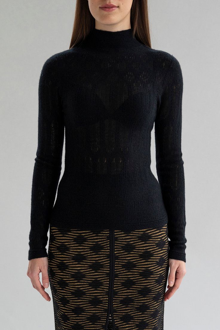 Woman wearing a slightly sheer black lace pointelle turtleneck pullover Black Stretch Cashmere Top, Elegant Stretch Pointelle Knit Top, Black High Neck Cashmere Top, Fitted Cashmere Top For Layering, Fine Knit Stretch Cashmere Top, Stretch Fine Knit Cashmere Top, Black Cashmere Funnel Neck Top, Fitted Fine Knit High Neck Turtleneck, Black Turtleneck Top With Sheer Sleeves