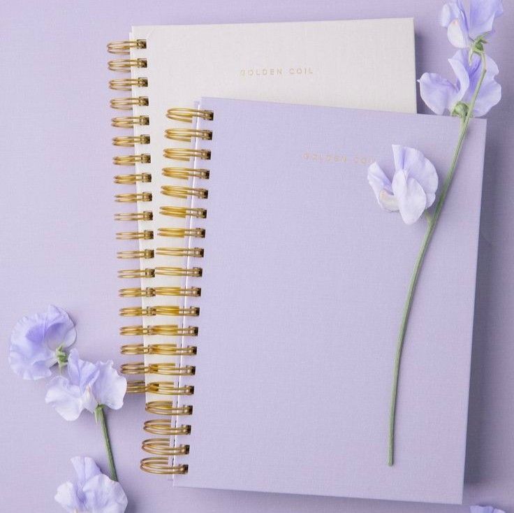 two notebooks with gold spiral binding and white flowers on the top one is empty