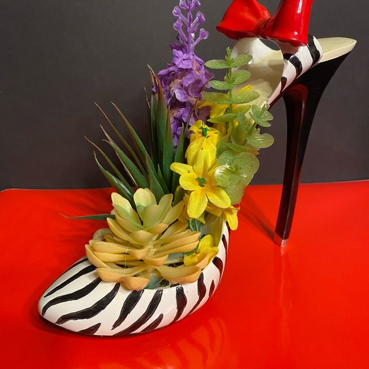 a zebra print shoe with flowers in it sitting on a table next to a pair of red shoes